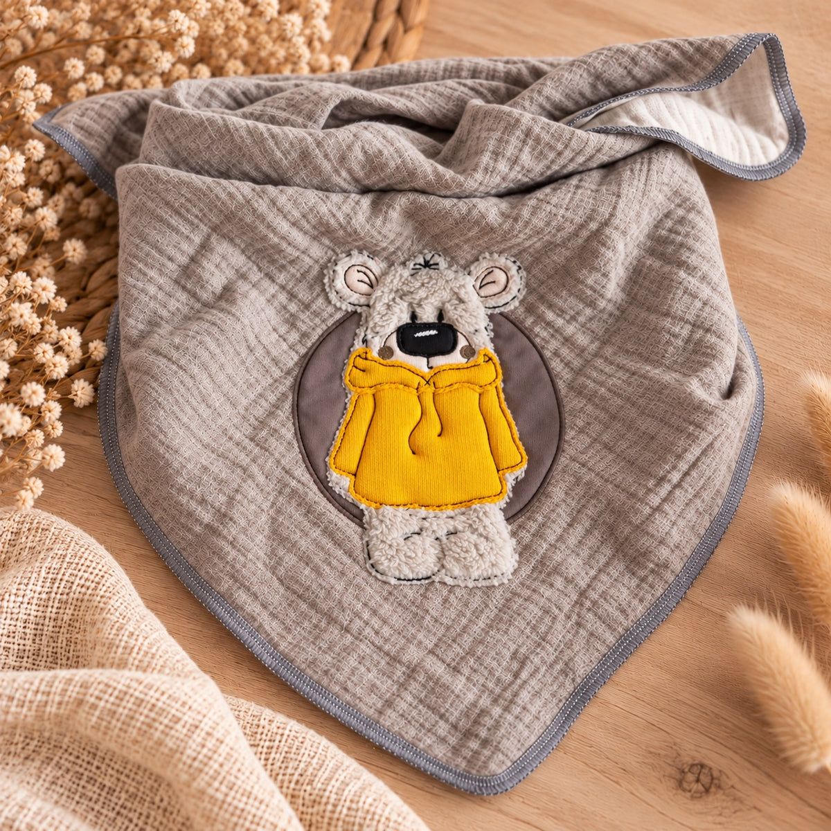 Helleres Gesamtfoto des graubeigen Musselin-Dreieckstuchs mit Teddy-Stickerei im senfgelben Hoodie